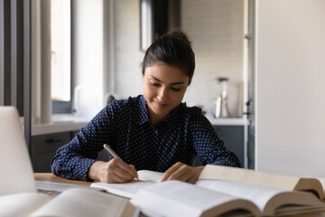 Close up Indian woman writing notes or essay, studying, reading textbook, smiling student sitting...