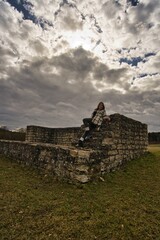 Eine Frau in einer gr&uuml;nen Leggings und einem karierten Hemd lehnt vor einem bew&ouml;lkten Himmel auf einer alten Mauer von dem R&ouml;merkastell in Pf&uuml;nz.