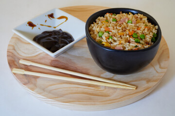 Delcious Special Fried rice in a bowl, soy sauce and Asian Chopsticks in round wooden plate