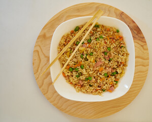 Delcious Special Fried rice in a white dish and Asian Chopsticks in round wooden plate. Top View