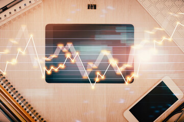 Double exposure of forex graph hologram over desktop with phone. Top view. Mobile trade platform concept.