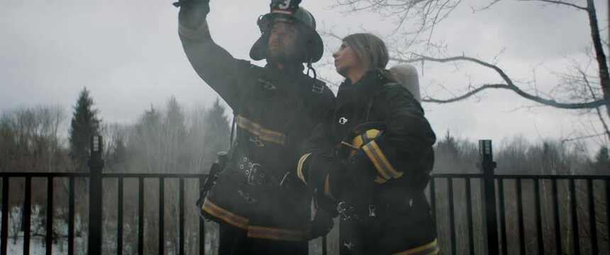 Two American firefighters in full gear discussing something in the smoke, preparing to fight fire. Shot with 2x anamorphic lens. 100 FPS slow motion