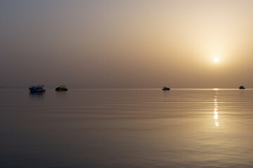 Obraz premium Dawn on the Red Sea in Egypt, Makadi Bay, calm sea, silhouettes of boats, golden disc of the sun on the horizon, reflection of sunlight on the water surface