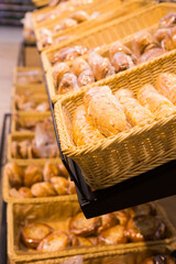 fresh golden breads with melted cheese wrapped in plastic wrap in wicker basket in bread department of supermarket
