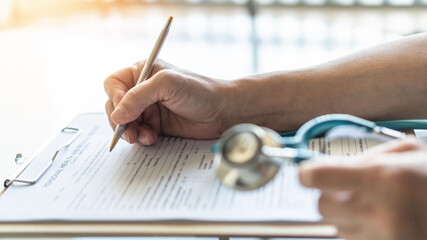 Medical doctor writing on patient personal health care record discharge form, or prescription...