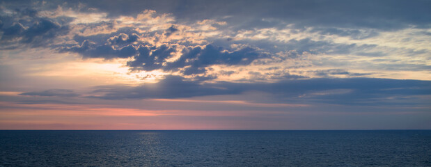 Panoramic view of a picturesque and dramatic sunrise sky over a vast and calm ocean.