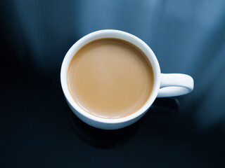 Coffee with milk in a white cup on a black glass background. Studio photography