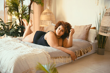 Beautiful curvy oversize African black woman afro hair lying on bed eco friendly bedroom cozy...