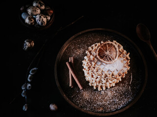 fresh waffles on a wooden plate, sprinkled with powdered sugar. waffles, quail eggs and nuts on a black background