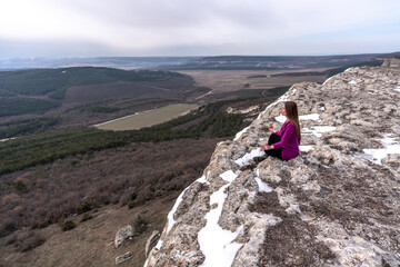 A beautiful woman sits in a lotus position on a high place with an amazing view of the mountains...