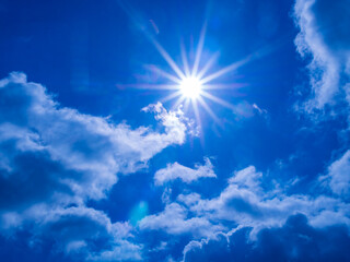 Clear sky with bright sun and rays in the atmosphere, below are light fluffy clouds