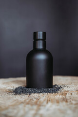 black cosmetic bottle packaging on black background on wooden table with black sand around