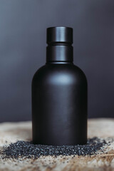 Luxury cosmetic black bottle packaging on black background on wooden table with black sand around from close up