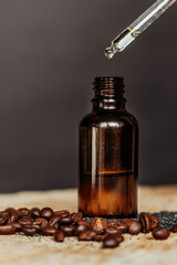 Drop falls from the pipette to  cosmetic oil bottle on a wooden table with coffee beans on black background.