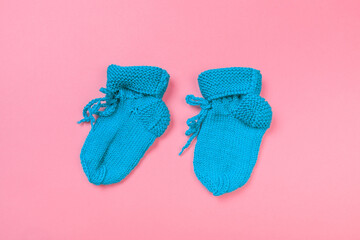 knitted baby booties on pastel pink background.