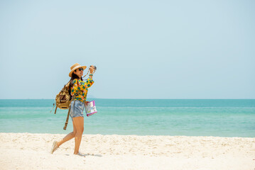 Asian woman traveler with backpack holding  map take photo on the beach enjoy life