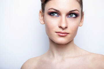 Front closeup portrait of a beautiful female model with bare shoulders with makeup, over light background.