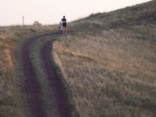 Obraz premium Textured road going uphill and a man with a bicycle in the distance.