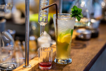 Close up the lemonade drink with ice in a clear glass beside a glass tube and the laboratory, adjust the flavor to the right, drink it, and refresh it, for sale in summer