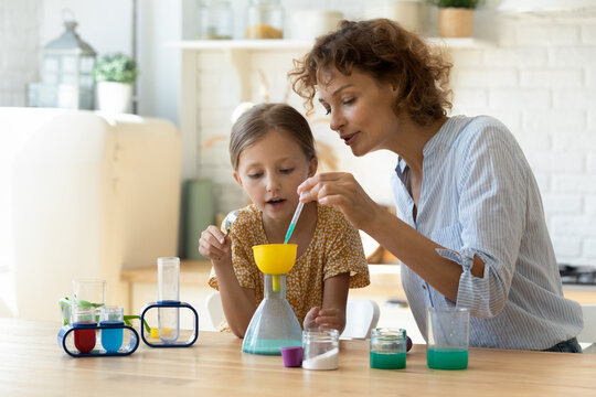 Excited young Caucasian mother and little 9s daughter have fun play with chemistry lab game together. Caring playful mom and small teen girl child engaged in interesting scientific activity at home.