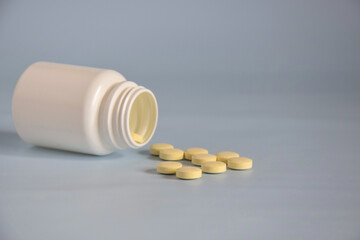 Pills in open upturned plastic jar. Medicine concept of drugs, tablets, medicines and pills on gray background. Copy space. Selective focus.