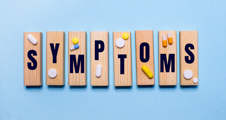 The word SYMPTOMS is written on wooden blocks on a light blue table near the pills. Medical concept