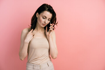 Fototapeta premium Portrait of a young woman on a pink background in a T-shirt of the same color. Attractive, smiling girl talking on a mobile phone.