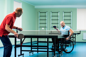 Fototapeta na wymiar Adult disabled man in a wheelchair play at table tennis with his coach