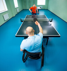Adult disabled man in a wheelchair play at table tennis with his coach