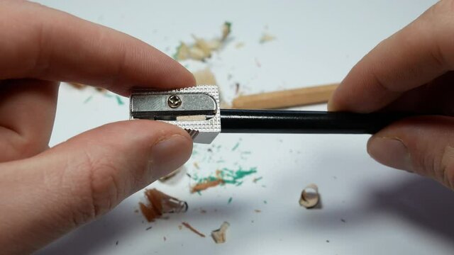 Man holding a sharpener in his hands and tries to sharpen broken pencil. He can't. Shavings and a graphite on white background. Close up.