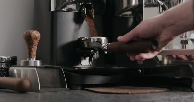 Slow motion man grinding fresh coffe in single spout portafilter with professional grinder