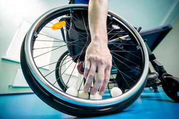 Disabled man in a wheelchair play at table tennis. Hand takes a ball fixed in a wheel
