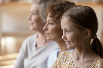 Close up of smiling three generations of Caucasian women look in distance think dream of future...