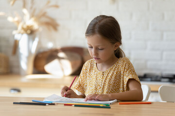 Smart little Caucasian 8s girl kid sit at table draw in album engaged in creative activity alone at home. Cute small teen 9s child have fun relax or study painting with pencils. Hobby, art concept.