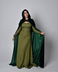 full length portrait of red haired girl wearing celtic, green medieval gown with fantasy velvet cloak. Standing pose isolated against a studio background.