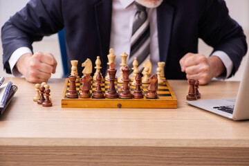 Old male employee playing chess at workplace