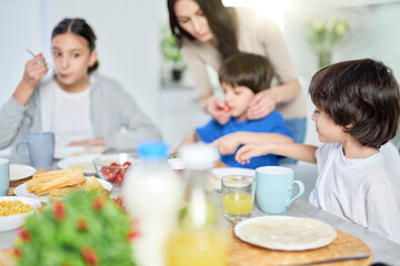 Obraz na płótnie Canvas Cute little hispanic boy having breakfast together with his mom and siblings. Latin family enjoying meal together, sitting at the kitchen table at home