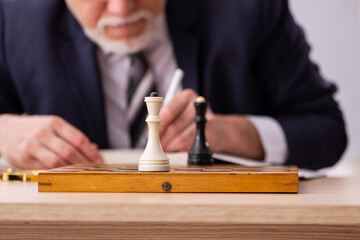 Old male employee playing chess at workplace