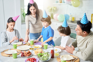 Preparation. Caring latin middle aged mother serving her family while they having dinner, celebrating birthday together at home