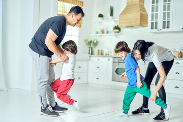 Fototapeta premium Active middle aged latin parents making two little boys do exercises in the morning at home. Healthy lifestyle