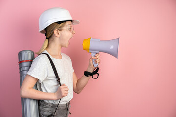 Portrait of a teenage girl in a helmet, a loudspeaker in her hands. Girl isolated on a pink background, shouting through a megaphone.
