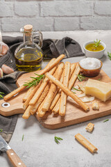 Traditional italian breadsticks grissini with rosemary, parmesan cheese, olive oil, garlic and salt on a gray background.