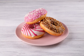 Three sugar-coated donuts are stacked on a pink ceramic plate on a light-colored wooden surface. Selective focus.