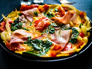 Breakfast - scrambled eggs with bacon and  vegetables on black wooden table

