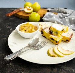 Sliced pie on a white plate with pear jam on a black table. Green pears in the background are blurred. Morning breakfast