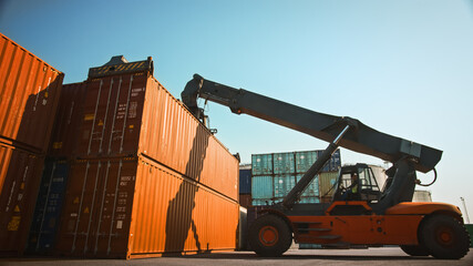 Modern Container Handler Carrying a Large Red Steel Shipping Cargo Storage Container in a Shipyard Terminal. Driver Operating the Handling Equipment is Loading the Crate in the Logistics Center.