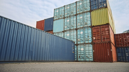 Low Angle Shot of an Industrial Terminal Location in a Shipyard Logistics Operations Center with Red and Blue Steel Shipping Cargo Containers. Daylight Cloudy Outdoors.