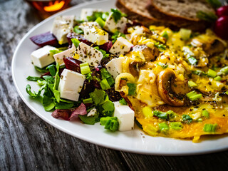 Continental breakfast - sunny side up eggs on white mushrooms, onion and greek salad on wooden table 