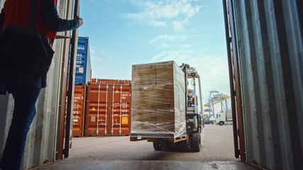 Forklift Driver Loading a Shipping Cargo Container with a Full Pallet with Carboard Boxes in...