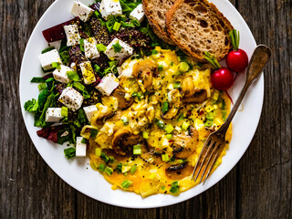 Continental breakfast - sunny side up eggs on white mushrooms, onion and greek salad on wooden table 